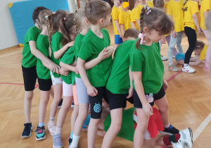 Dzieci stoją w rzędzie i przechodzą pod nogami kolegów