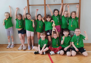 Dzieci z medalami i pucharem pozują do zdjęcia na tle drabinek